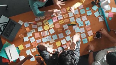 Top view of business team giving high five to celebrate project while standing at table with sticky notes and laptop. Aerial view of designer clapping hands to congratulate successful idea. Symposium.