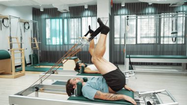 Müşteri, spor salonundaki yenilikçi bir makinede kayışla ters bacak kaldırma hareketi yapıyor. Çekirdek bağlantısını, dengesini ve esnekliğini geliştirmek için ters takla atan iki mutlu antrenör. Alışkanlık.