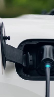 Ön görüş EV şarj cihazı, elektrik yükleme istasyonundan parlayan ışık kablosu ile elektrik yüklemek için elektrikli arabaya takıldı. Kesme-Sınır yeniliği ve gelecekteki yeşil enerji sürdürülebilirliği. İnceleyin