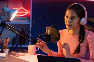 Geceleri podcast 'te olumlu konuşmalar yapan, pembe neon ışıklı modern stüdyoda sunum için dizüstü bilgisayar kullanan, gülümseyen, genç, güzel Asyalı bir etkileyiciydi. Taktik.