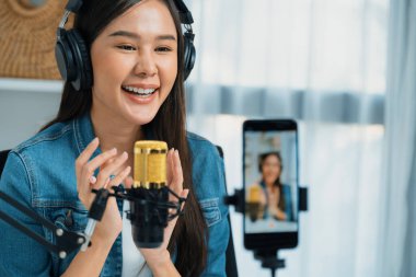 Asyalı sunucu canlı yayında canlı yayında canlı yayında sosyal medyada kulaklık takarak konuşuyor. Dinleyicileri modern stüdyoda koçluk yaparak selamlıyor. Taktik.