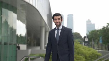 Profesyonel iş adamı hareket ediyor ve kameraya bakarken ayakta duruyor. Gülümseyen yönetici kameraya kendinden emin bir şekilde gülümsüyor. Mimari binada takım elbiseli yatırımcıların yakın çekimi. Sevinçli..