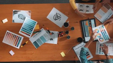 Proje yöneticisi renk paletleri seçerken tasarımcının tablete baktığı yukarıdan aşağıya hava görüntüsü. Profesyonel grafik tasarımının en üst görüntüsü ve logoya bakın. Yetenekli ekip grafikleri seçiyor. Sempozyum.