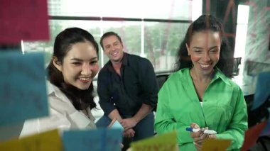 Profesyonel iş adamları, cam duvarda yaratıcı fikirleri paylaşmak için yapışkan notlar kullanarak pazarlama fikrini araştırıyor. Bir grup farklı iş adamları strateji hakkında tartışıyorlar. - Yakın çekim. Yönlendirici.