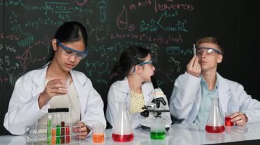 Akıllı genç kız kimya teorisi ile tahtayı dikkatlice incelerken mikroskop altında numune bırakıyor. Profesyonel bilim adamı tüpün içine kimyasal madde döker ve deney için hazırlanır. Öğretim