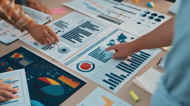 Çeşitli bir iş ekibi toplantı sırasında veri analizi yapar. Modern ofis ortamında bilinçli stratejik kararlar almak için grafikler ve çizelgeler keşfediyorlar. SACTR
