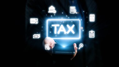 Bir kişi, finans, bütçe ve vergilendirme yönetimine çağdaş yaklaşımı yansıtan, karanlık bir zemin karşısında aydınlatılmış vergi sembolleri içeren bir akıllı telefon sergisi tutuyor. Dörtgen