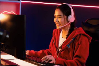 İnternet üzerinden kulaklık takıp gülümseyen Asyalı güzel kız flamasının sunucu kanalı izleyicilerle internet üzerinden konuşma yapıyor. Esport yetenekli takım oyuncuları neon mavi odada. Taktik.