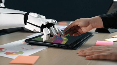 İnsan elinin dijital tablet üzerindeki robot eliyle etkileşime girdiği çarpıcı bir sahne, teknolojinin yaratıcı süreçler ve takım çalışmalarına entegrasyonunu simgeliyor. Noogenesis