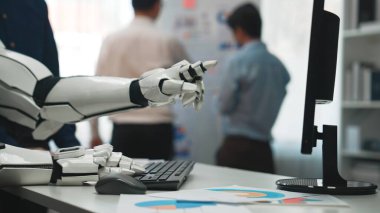 Gelecekçi bir robotik el bir bilgisayar klavyesine bağlanır, profesyoneller arka planda işbirliği yaparken, teknolojinin iş akışlarına entegrasyonunu gösterir. Noogenesis