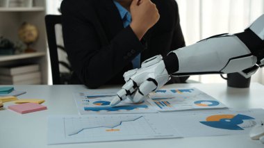 Bir robot kolu, otomasyon ve teknolojinin modern çalışma alanına entegrasyonunu gösteren bir iş toplantısı sırasında grafikler ve grafiklerle uğraşır. Noogenesis