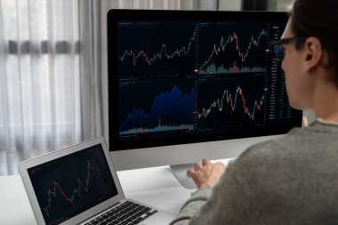 Stresli iş adamı günü modern ofisteki dinamik borsa grafiğine bakıyor, veri tabanı bilgisayarını ve bilgisayarını evden çalışırken karşılaştırıyor. Bireysel.