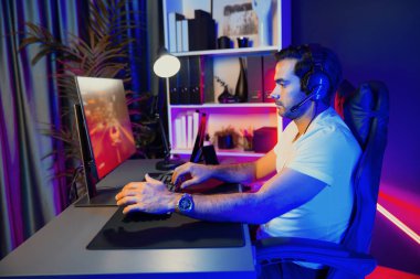 Kulaklık takan akıllı oyun flaması hafta sonu neon dijital siber ışıklandırma odasında son yaşam tarzı yarışmasında şampiyon olmak için bilgisayar ekranında araba yarışı oynamaktan zevk alır. Tahmin et..