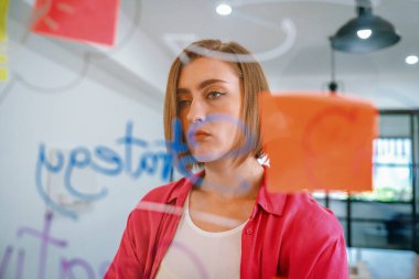 Yaratıcı iş toplantısında cam panonun önünde yapışkan notlar ve zihin haritasıyla dururken kafası karışık düşünen beyaz iş kadınının portresi. Tertemiz..
