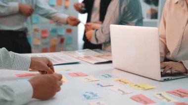 Takım çalışması ve yaratıcılığı vurgulayan yapışkan notlar ve dizüstü bilgisayar kullanarak canlı bir beyin fırtınası yapan modern bir ofis sahnesi. SACTR