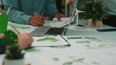 Yesil proje planlarini tartisan, dizüstü bilgisayarlar, bitkiler ve grafiklerle birlikte, ekip çalismalarinin ve yeniligin vurgulandigi, canli bir is gorusmesi sahnesi uzmanlariyla gorusuyor. SACTR