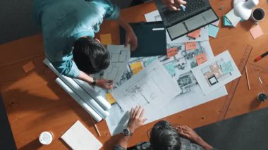 Yetenekli iş adamlarının tablet tutması ve planlara bakması. Masada dizüstü bilgisayarla dururken mimarın tasarım ve planlama bölümünün havadan görüntüsü. Sempozyum.