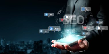 Bir işadamı, dijital pazarlama stratejilerinin önemini vurgulayarak, şehrin ufuk çizgisine kurulmuş SEO ve sosyal medya katılım ölçümlerini gösteren bir akıllı telefon sergiliyor. XDMCP