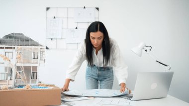 Genç, güzel beyaz bir mimar masanın üzerine plan koyar ve ev modeliyle karşılaştırırken, modern ofisteki fahişe modellerini dikkatlice incelerken arkadaki çizgilerle karşılaştırır. Tertemiz..