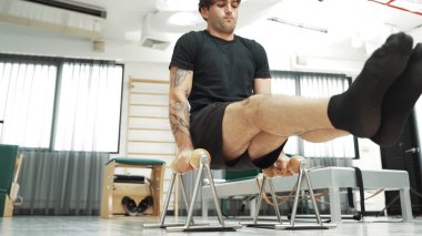 Spor salonunda vücut kontrolünü ve çekirdek gücünü arttırmak için pilates reformcusu üzerinde L-sit egzersizi yapan bir adam. Sportif adam, çekirdek, kol ve omuz güçlendirmek için yenilikçiyi sıkıştırıyor. Alışkanlık.