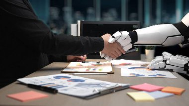 İnsan eli, modern bir ofiste ortaklığı temsil eden robotik bir elle titrer. Çizelgeler ve kağıtlar gibi görsel öğeler yenilik ve işbirliği temalarını vurgular. Noogenesis