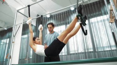Pilates eğitmeni, Cadillac teçhizatı üzerinde asılı duran bir bacak egzersizinde bir müşteriye rehberlik ediyor. Vücut dengesini sağlamak için Cadillac 'ı geren sağlıklı bir kadın. Alışkanlık.