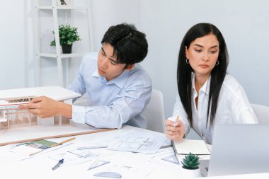 Profesyonel Asyalı erkek mimar ev modelinin uzunluğunu ölçmek için cetvel kullanırken, beyaz tenli genç meslektaşı ev modeliyle toplantı masasındaki verileri analiz etmek için dizüstü bilgisayar kullanıyor. Tertemiz..