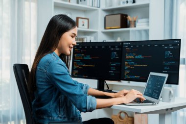 IT geliştiricisinde gülümseyen genç Asyalı dizüstü bilgisayarında kodlama programı verileriyle kotlu tişört giyerek çevrimiçi bilgi yazıyor. Güvenlik analizi iki ekran ile çevrili. Taktik.