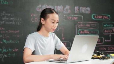 Kara tahtada dizüstü bilgisayar kullanarak akıllı kız programlama sistemi. Lise öğrencisi mühendislik kodları yazıyor ya da STEM teknoloji sınıfındaki kameraya bakarken bir şey söylüyor. Yaratıcı eğitim. Öğretim