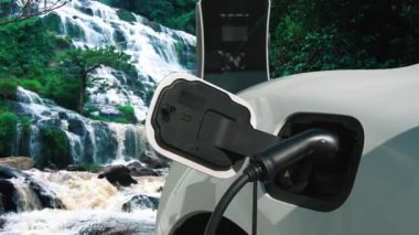 Elektrikli araba, doğal ortam, şelale ve akış arkaplanındaki şarj istasyonundan enerji yüklüyor. Yenilenebilir enerji kaynaklı EV otomobillerin enerji sürdürülebilirliği kavramı.