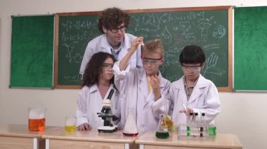 Amerikalı bir kız renkli sıvıyı incelerken erkek beher içine solüsyon döker. Enerjik öğrenci, öğretmenler çocukları keşfederken ve yenilikleri keşfederken arkadaşının deney yapmasına destek oluyor. Pedagoji.