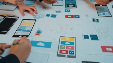 Dinamik bir çalışma alanı, hareketli fikirler ve araçlarla dolu bir masada ellerin mobil planlar ve dijital prototipler çizdiği işbirlikçi bir tasarım süreci sergiliyor. SACTR