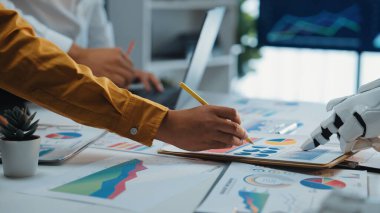 Yenilikçi çözümler için çizelge ve grafiklere yardımcı olan bir robotun yer aldığı, iş dünyasından bir ekibin veri analizinde işbirliği yaptığı dinamik bir ofis. Noogenesis