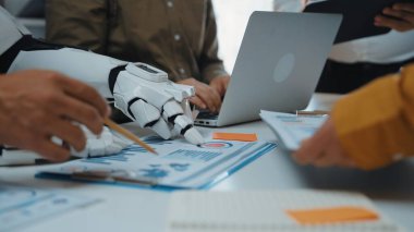 İnsansı bir robot modern bir ofiste insan meslektaşlarıyla işbirliği yapıyor, stratejik bir iş toplantısı sırasında verileri inceliyor ve fikirler sunuyor. Noogenesis