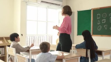 Çeşitli öğrenci ödevlerini kontrol ederken etrafta dolaşan ve etrafa bakan beyaz bir öğretmen. Çok kültürlü çocukların okuması ve dinlemesi ilkokuldaki sınıfta fikrini açıklıyor. Pedagoji.