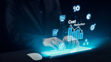 Bir işadamı, günümüz iş yerinde modern finansal analizleri temsil eden, interaktif maliyet azaltma simgeleri ve grafikleriyle çevrili, fütürist dijital bir klavyeyle ilgilenir. Dörtgen