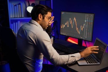 Akıllı tüccar işadamı, karanlık oda gecesinde neon ışıklı ofisteki arama pazarında yüksek kârla ekranda bilgisayar ve bilgisayar üzerinde dinamik borsa yatırımları üzerinde yoğunlaşıyor. Tahmin et..