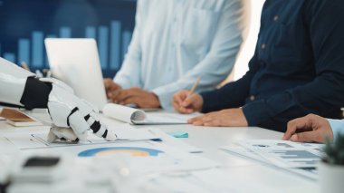 Bu resim modern ofis ortamında profesyonellerle işbirliği yapan, teknoloji ve insan etkileşiminin iş süreçlerinde entegrasyonunu vurgulayan bir robotu tasvir ediyor.