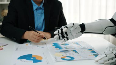 Bir iş adamı ve bir robot veri analizi, modern ofis ortamında grafik ve çizelgeleri incelemek, yenilik ve takım çalışmasını ön plana çıkarmak konusunda işbirliği yaparlar.