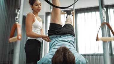 Cadillac ekipmanları üzerinde bacak kaldırma egzersizinde müşteriye yardımcı olan yetenekli pilates eğitmeni. Kadın antrenör, Cadillac 'ın bacak gerdirme hareketine yardım ediyor. Temel bağlantıyı geliştirmek için, bacak esnekliği için. Alışkanlık.