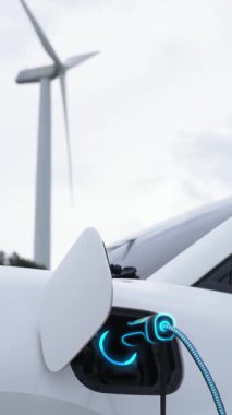 Elektrikli araba, rüzgar türbini çiftliğinde çalışan akıllı EV şarj cihazıyla şarj edilen enerjiyi şarj ediyor. Alternatif temiz sürdürülebilir enerjinin teknolojik ilerlemesi. İnceleyin