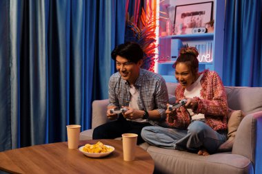 Neşeli, gülümseyen bir çiftin koltuğunda oturup oyun oynuyorlar. Oyun konsolu, hazır aperatifler ve içecekler, modern neon ışıklı, rahat oturma odasında eğlenceli bir rekabet seviyesinde. İnfobahn.