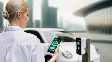 EV akıllı telefon uygulamasında EV akü durumu. Kamu şarj istasyonundan şarj olurken. EV arabaların yenilikçi teknolojik gelişimi ve alternatif enerji kullanımı. İnceleyin