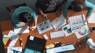 Takım ayakta dikilirken ve yorum yaparken müdürün fikir yazma konusunda üst düzey görüşü. Profesyonel tasarımcı logosu renk paletine bakarken ve renkli kalemle fikri kağıda yazarken. Sempozyum.