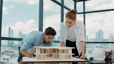 Profesyonel kooperatif iş arkadaşı ev modelini incelerken kalem kullanarak mimari modeli işaret eden yetenekli proje yöneticisi. Mimar mühendis takımı modeli belirlemek için birlikte çalışıyor. İzleme