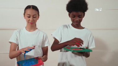 Beyaz kız ve Afrikalı çocuk ellerini suluboya kırmızıya bandırıyor - mavi ya da kontrastlı renge ve sanat dersinde beyaz duvarı damgalamak için geri dönüyorlar. Yaratıcılık aktivite konsepti. Öğretim