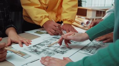 Modern bir ofiste çeşitli profesyonellerden oluşan bir grup, mimari planları ve tasarımları inceleyerek takım çalışmalarını ve yaratıcı çözümleri destekliyor. SACTR