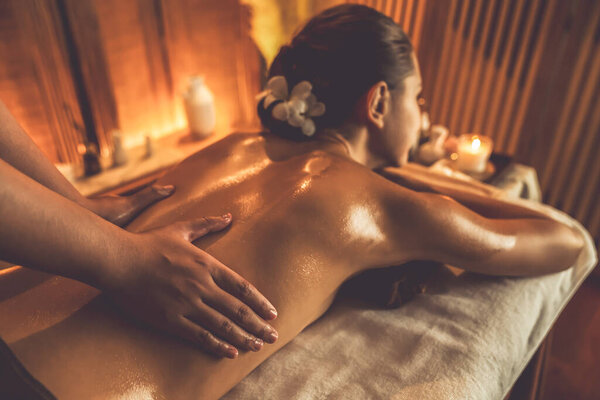 Caucasian woman customer enjoying relaxing anti-stress spa massage and pampering with beauty skin recreation leisure in warm candle lighting ambient salon spa at luxury resort or hotel. Quiescent