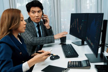 Gülümseyen Asyalı işadamı komisyoncu dinamik borsa veritabanını arıyor. Kadın iş ortağı, iç işyerindeki kar eden uygulama programını karşılaştıran ekranlara işaret ediyor. İnfobahn.