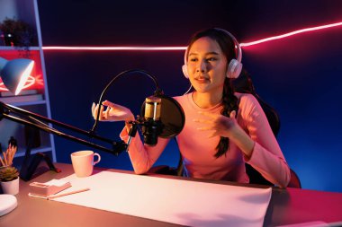 Geceleri podcast 'te olumlu konuşmalar yapan, pembe neon ışıklı modern stüdyoda sunum için dizüstü bilgisayar kullanan, gülümseyen, genç, güzel Asyalı bir etkileyiciydi. Taktik.